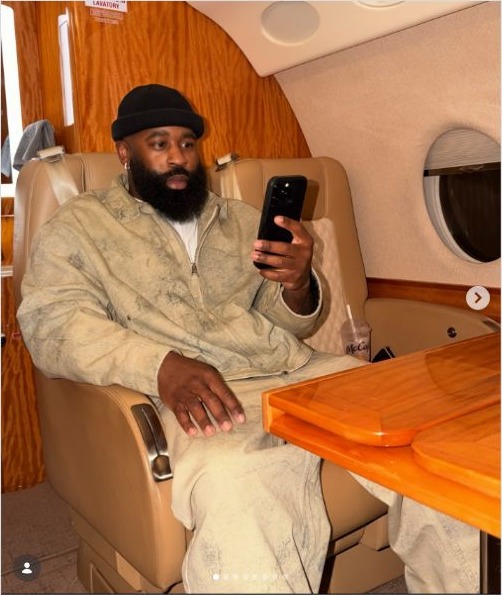 TC Cooper in a gray outfit seated inside a private jet